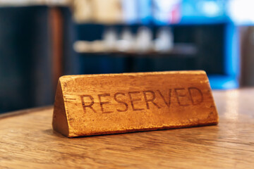 Close-up of a rustic wooden "Reserved" sign placed on a wooden restaurant table, with soft bokeh background