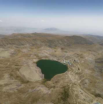 Aerial view of the serene, dark waters of Lake Kari nestled among the rugged, arid mountains under a hazy sky, Lake Kari, Aragatsotn Province, Armenia.