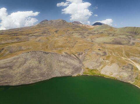 Aerial view of the vivid green waters of Lake Kari nestled against the rugged, ochre-toned slopes of Mount Aragats, Lake Kari, Aragatsotn Province, Armenia.