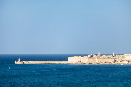 Saint Elmo Breakwater and lighthouse extending into blue Mediterranean waters, with historic limestone coastal fortifications