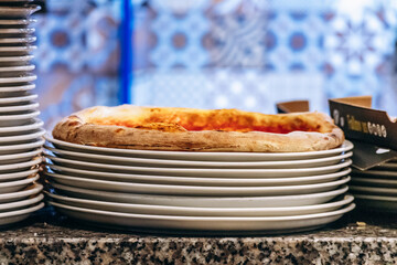 Fresh pizza resting on stacked white plates at restaurant counter
