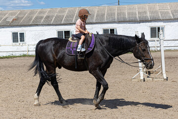 Little girl riding a horse alone in outdoor arena