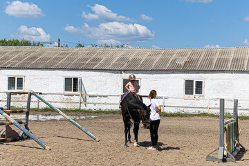 Little girl learning horseback riding with trainer on farm arena