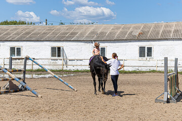 Little girl learning horseback riding with trainer on farm arena