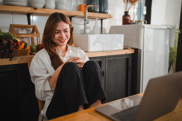 Young woman drinking milk and using laptop in kitchen