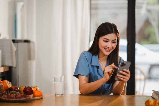 Young woman using smartphone while having breakfast in modern kitchen