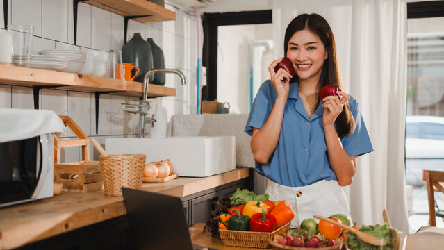 Young woman holding apples and smiling in kitchen with fresh produce