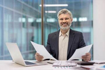 Obraz premium Smiling business professional reviewing documents at a modern office desk.