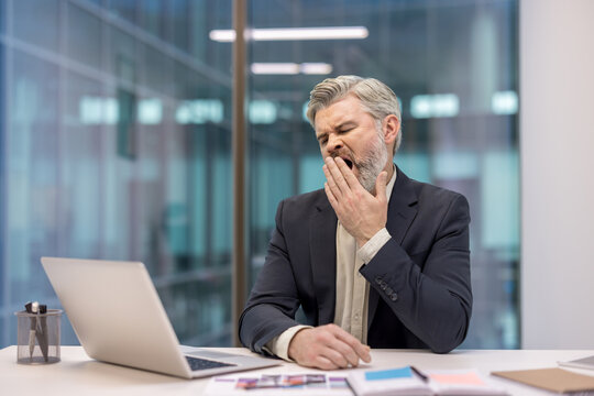 Tired businessman yawning at his desk during a busy workday in an office