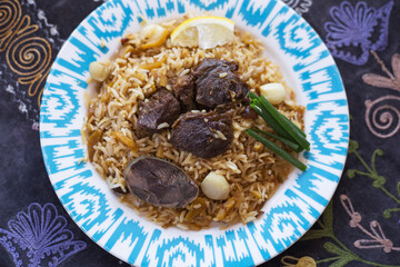 Top view of a plate with National Uzbek pilaf with pieces of lamb, green onion. Central Asian traditional cuisine. Lifestyle background.