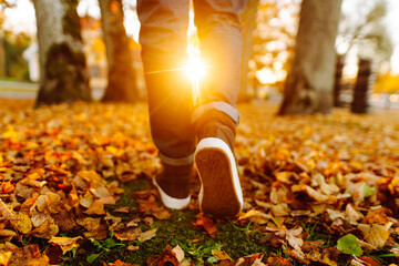 A close-up of a man in boots walking along a path strewn with bright autumn leaves. A man in shoes walks in an autumn park on a sunny day. The concept of seasonality, walks.