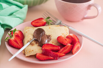 Crepes with chocolate spread and fresh strawberries, served with tea on pink background