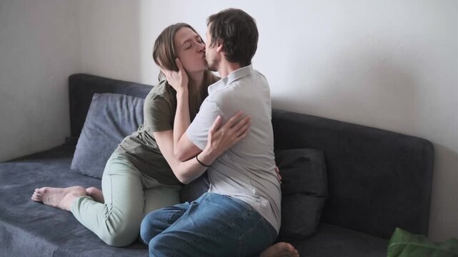 Romantic young couple passionately kissing while embracing on cozy sofa at home, loving mood