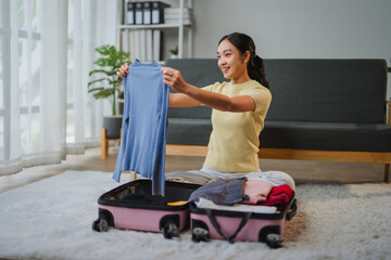 Young woman packing clothes in suitcase, preparing for travel at home