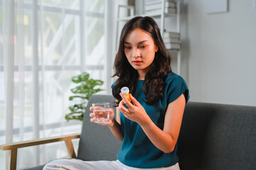 Young woman taking medicine at home sitting on the sofa