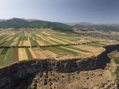Aerial view of golden and green fields contrasting against the rugged cliff edges, creating a picturesque landscape with mountains in the background, Lori, Lori Province, Armenia.