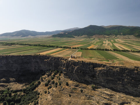 Aerial view of a serene plateau edge overlooking a valley with patterned fields, contrasting the rugged cliffside with the orderly landscape, Lori, Lori Province, Armenia.