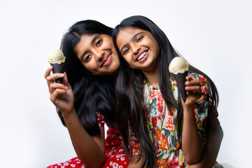 Cute Indian sisters enjoying ice cream cones in colorful frocks against a clean white backdrop