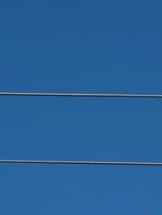 Two wires against a clear blue sky on a sunny day with no birds present