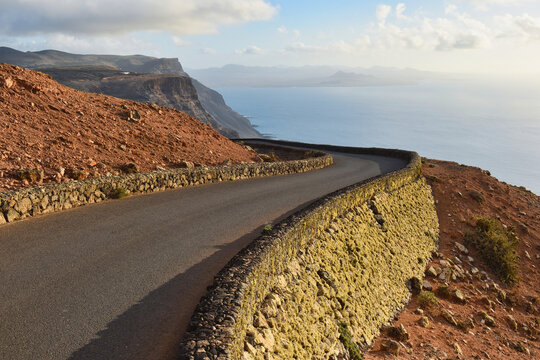 Scenic winding coastal road in Lanzarote Canary Islands with dramatic volcanic cliffs, stone walls, and breathtaking ocean views at sunset, vacation destination - Powered by Adobe