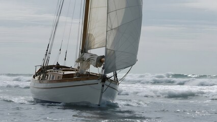 Sailboat navigating through choppy ocean waters under a cloudy sky