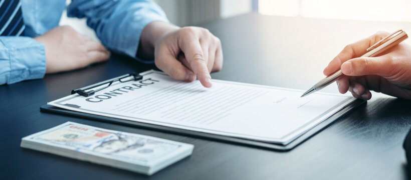 Man employee giving bribe banknote to businessman and pointing at the contract signing box while he is holding pen