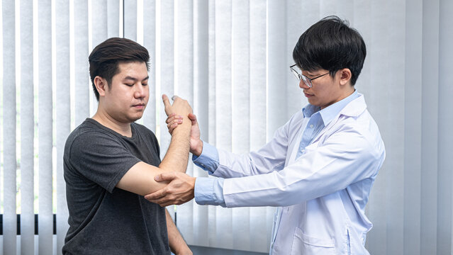 Young asian physiotherapist giving assistance to man patient with elbow injury