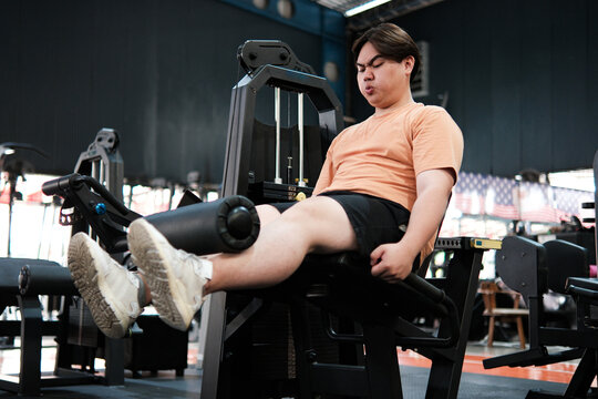 Overweight man exercising on a leg extension machine at the gym, focusing on lower body strength and endurance.