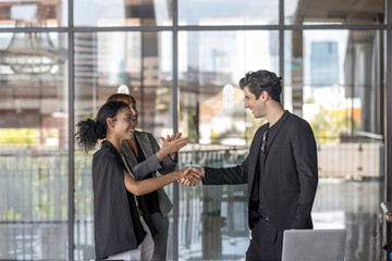 Two business team members reach an agreement and have handshake in front of a senior manager outside of the building. Partnership and collaboration between young business team members