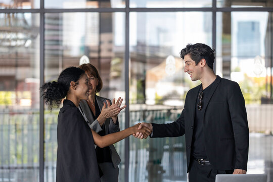 Two business team members reach an agreement and have handshake in front of a senior manager outside of the building. Partnership and collaboration between young business team members