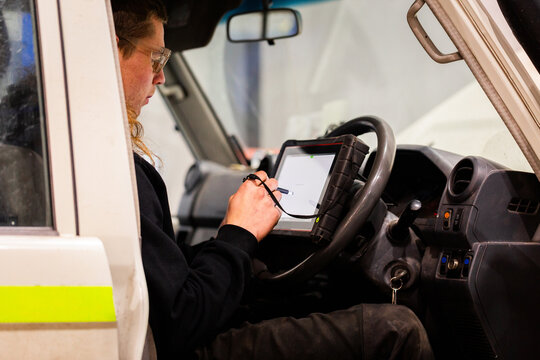 tradesman mechanic with diagnostic device running tests on old mining fleet vehicle in workshop
