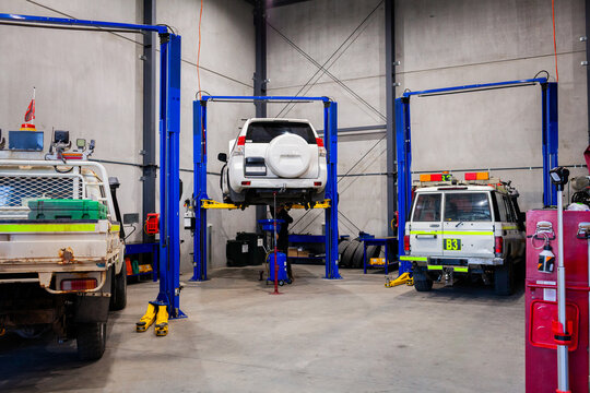Young male mechanic working on the undercarriage of white SUV on car lift inside workshop