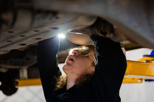 Young male mechanic working on the vehicles underbody with flashlight on