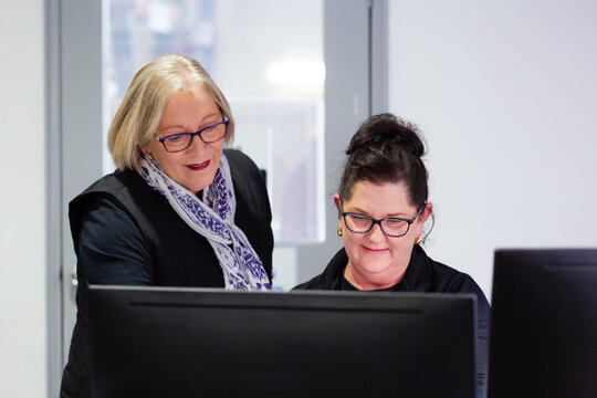 Two female office workers looking at a desktop computer at work together