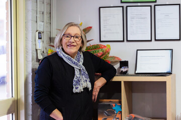 Female businesswoman standing by  wooden shelf with framed business awards and qualifications