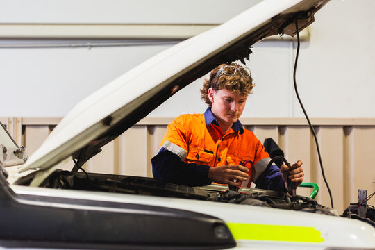 Young male mechanic working on white vehicle with bonnet opened