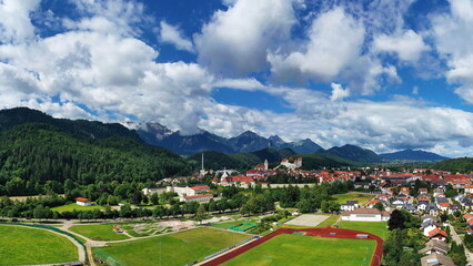 Sportanlage mit Fußballfeld, Laufbahn und Baseballplatz vor idyllischer Bergkulisse bei Füssen – eingebettet in grüne Natur mit Hügeln und Wolkenstimmung.