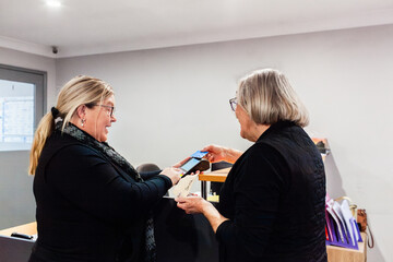 Female office staff showing holding eftpos machine for payment from businesswoman client