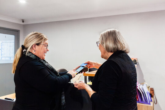 Female office staff showing holding eftpos machine for payment from businesswoman client