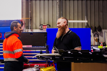 diverse mechanic workmates chatting together in industrial shed workspace