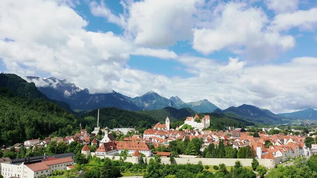 Das Foto zeigt die charmante Altstadt von F&uuml;ssen mit ihren roten D&auml;chern, liebevoll restaurierten Fassaden und dem markanten Turm der Kirche St. Mang. Im Hintergrund erhebt sich das beeindruckende Alp