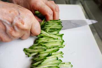 Close-up of senior woman’s hands slicing cucumber into thin strips