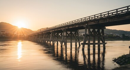 Obraz premium Scenic view of old wooden bridge spanning a river during sunset, reflecting in the water.
