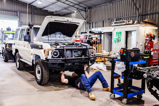 tradesman mechanic with installing bullbar on new vehicle in workshop lying under car