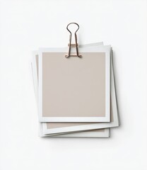 Stacked, light beige, square photo prints, held by a rose gold binder clip, on a white background