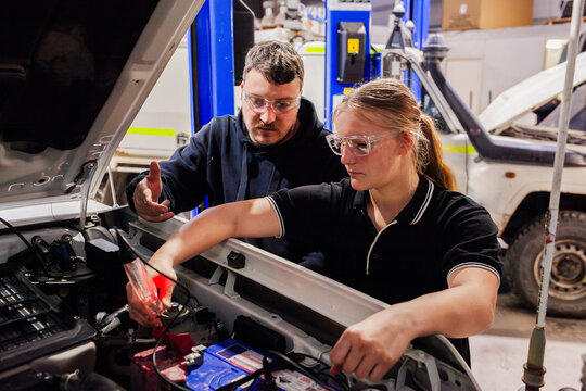 female mechanic tradeswoman working on car repair in industrial workshop with supervisor helping