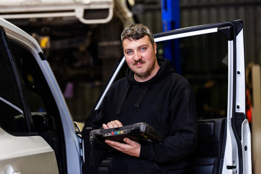 tradesman mechanic with diagnostic device testing vehicle in workshop