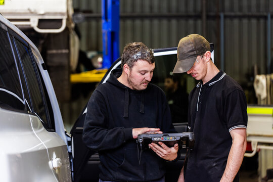 tradesman mechanic with diagnostic device chatting with apprentice workman in industrial shed