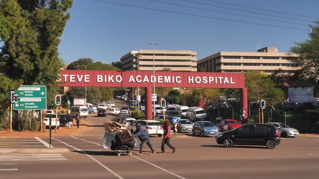 Informal trash picker pushes cart laden with recyclable materials across intersection by Hospital entrance
