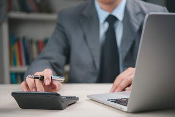 Businessman using calculator and laptop in office, working on financial report, accounting, business management, investment planning, tax calculation, corporate finance and data analysis.